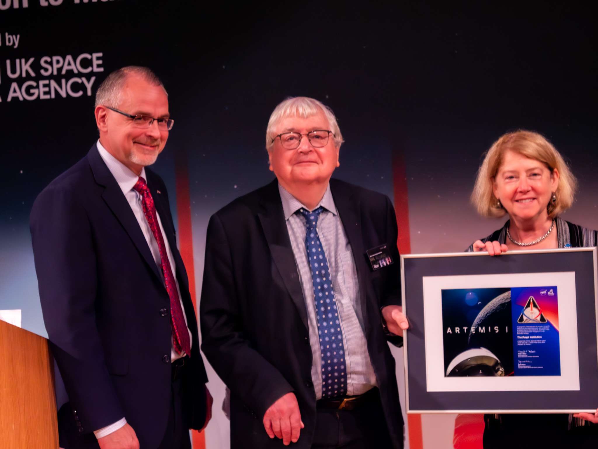 NASA Deputy Administrator Pam Melroy and Associate Administrator for the Exploration Systems Development Mission Directorate Jim Free presenting the Chair of the Board of Trustees of the Royal Institution, Sir Richard Catlow, with a space-flown mission patch from the Artemis I mission.