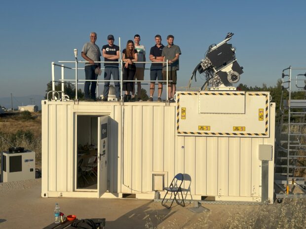 Group of six people on top of a cargo container with satellite technology on the roof.